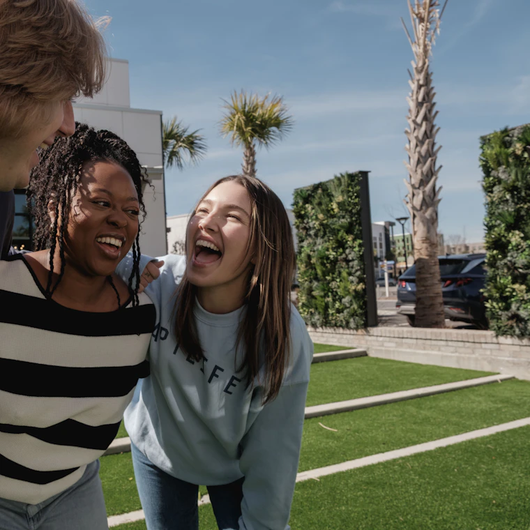 Three colleagues laughing together outdoors on a sunny day
